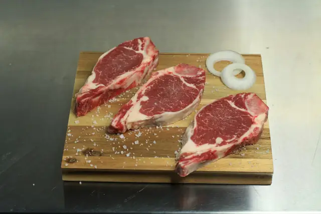 Tres cortes de carne cruda presentados sobre una tabla de madera.