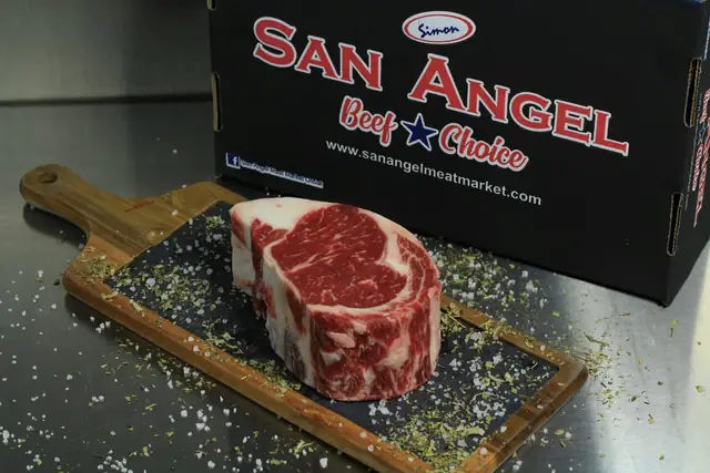 Corte de carne cruda sobre una tabla junto a un empaque de San Angel Meat Market.